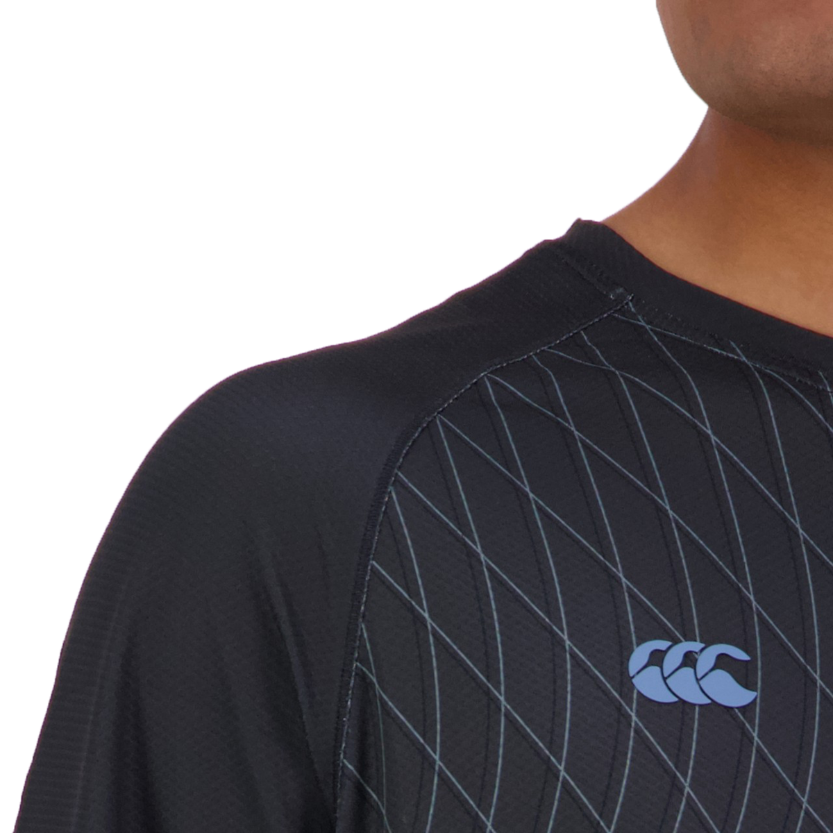 A person wears the Canterbury Tempo+ AOP Training Tee, which is black with blue stitching and a blue CCC logo. Made from moisture-wicking fabric, it enhances comfort during intense workouts, and its reflective detailing adds a stylish touch.