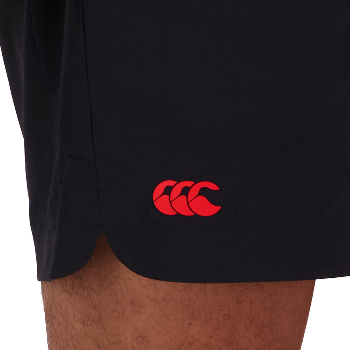 A person wears Canterbury Everest 5" Woven Short in black, showcasing a red logo with three overlapping curves near the hem. Made from four-way stretch fabric, these shorts ensure enhanced flexibility and quick-drying for ultimate comfort.