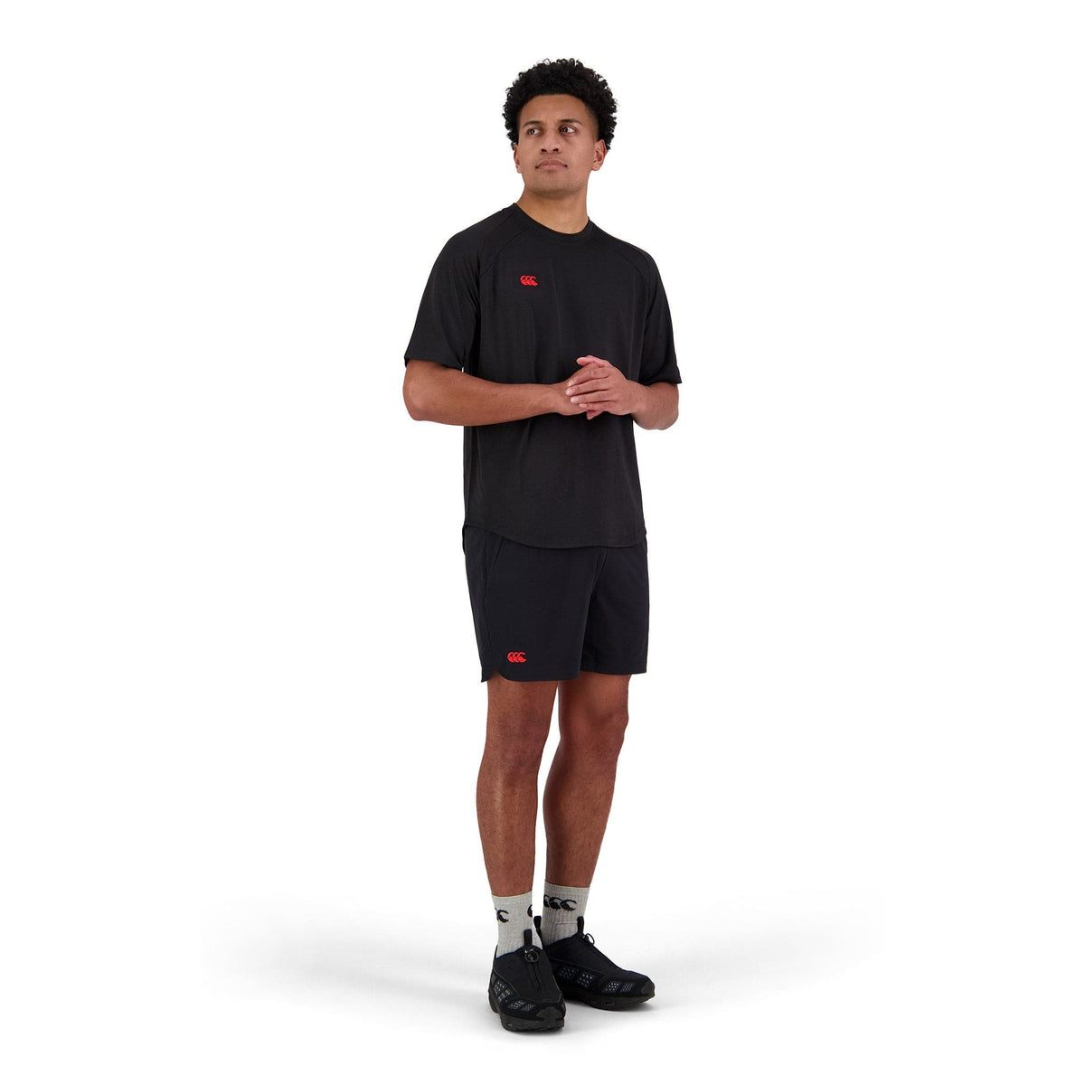 A man in a black Canterbury Everest 5" Woven Short, crafted from quick-drying fabric, stands with hands clasped against a white background.