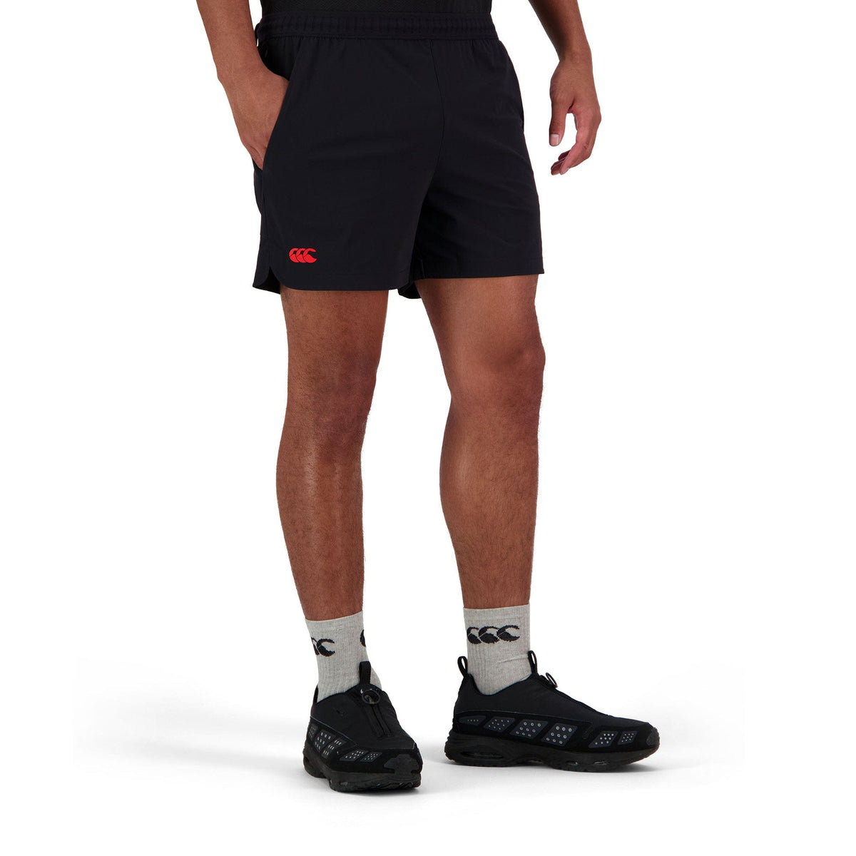 The individual is wearing the Canterbury Everest 5" Woven Short in black, paired with logo'd gray socks and black shoes, set against a white backdrop.