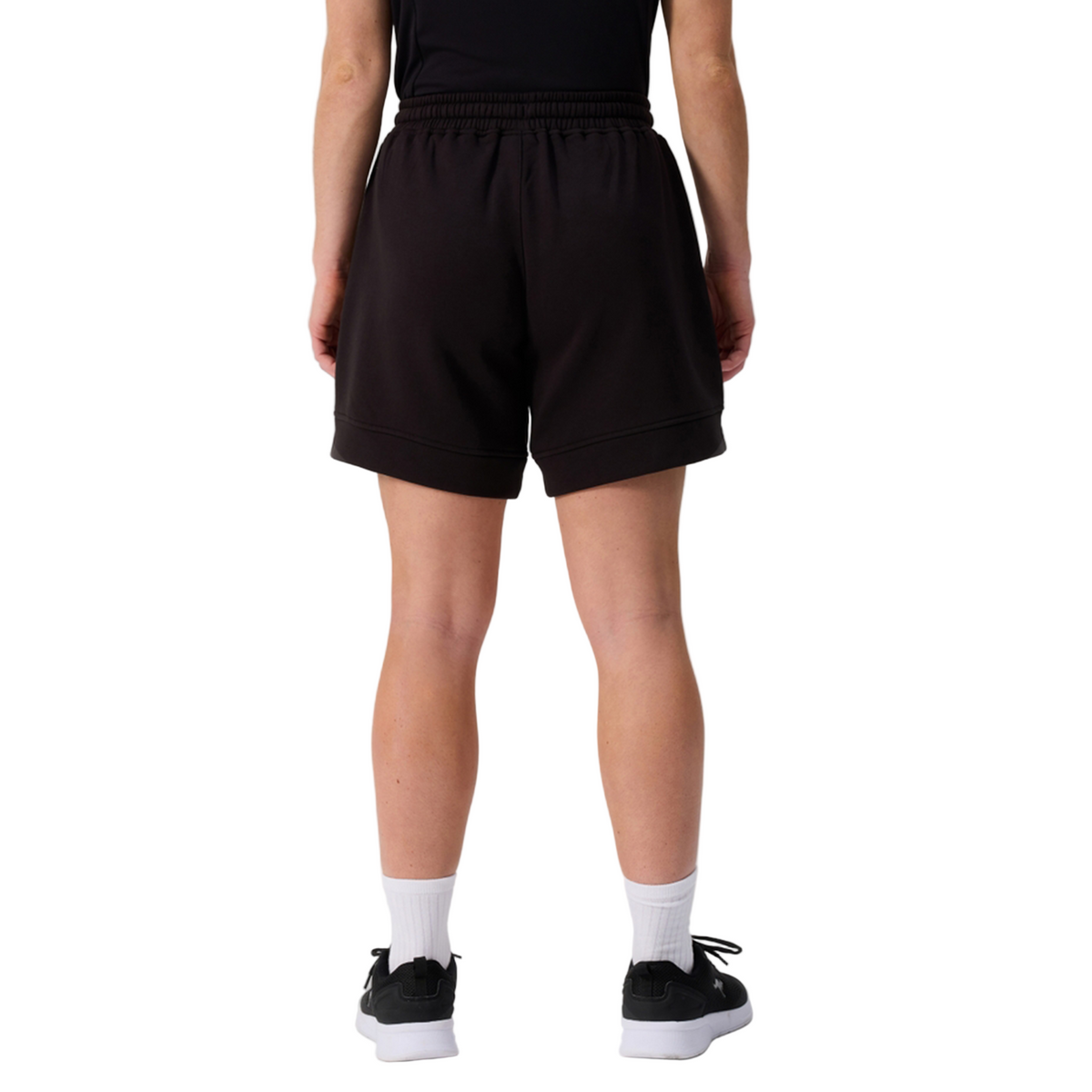 A person shown from the waist down, facing away, wears Canterbury Women&#39;s Ireland 25/26 Knit Short, a black shirt, white socks, and black sneakers against a white background.