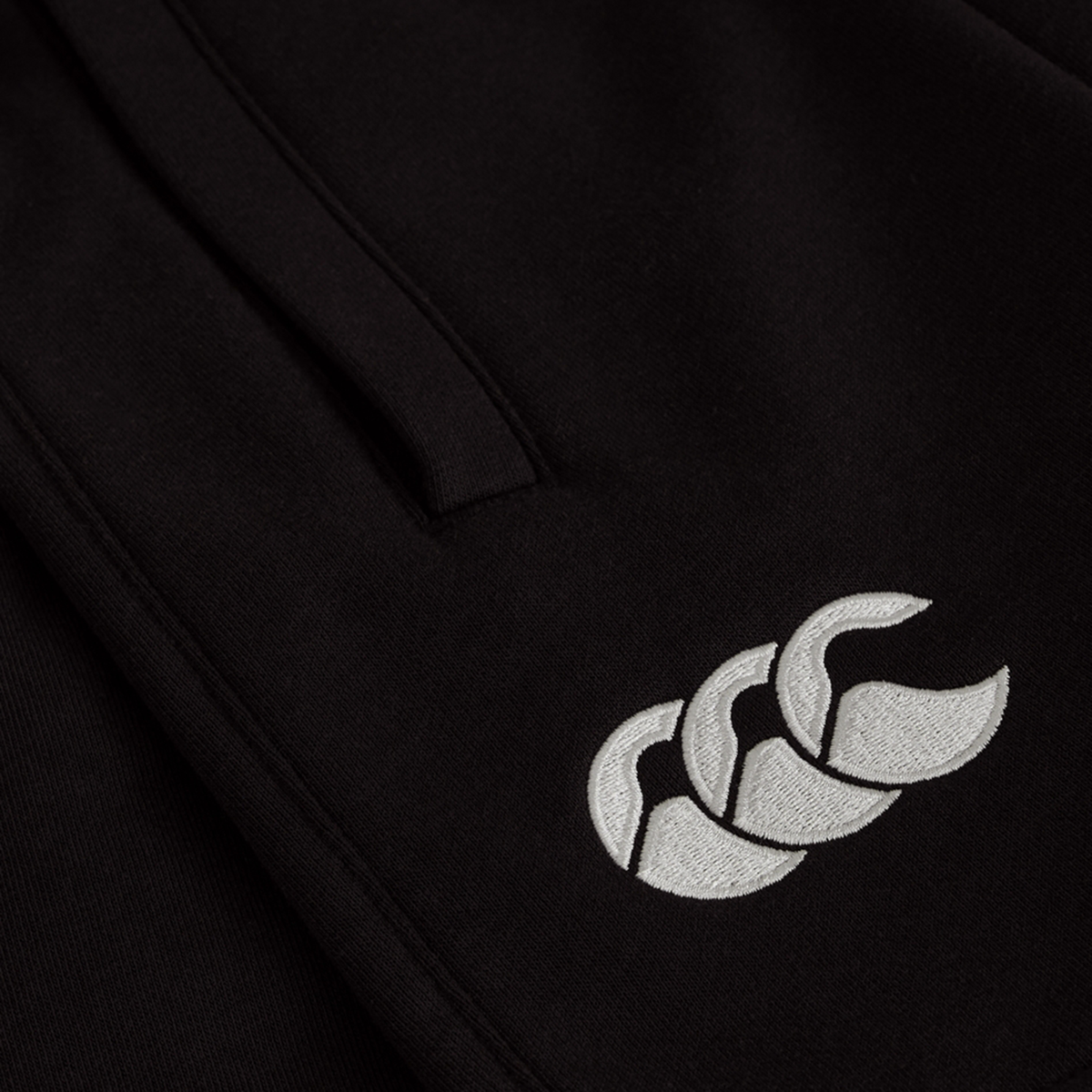 Close-up of the Women&#39;s Ireland 25/26 Knit Short by Canterbury, showing a white embroidered triple-shape logo on black fabric. Perfect addition to women&#39;s sports shorts collections.