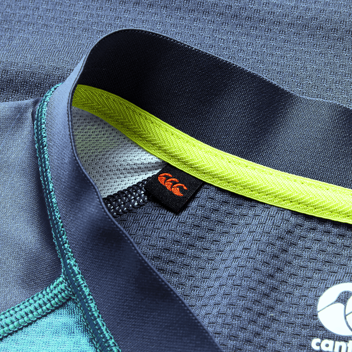 Close-up of the Ireland 26/27 Summer Tour "Baltic" Training Test Jersey by Canterbury in blue with yellow-green trim, mesh fabric, and a black tag with an orange logo—perfect for supporting your team this summer.