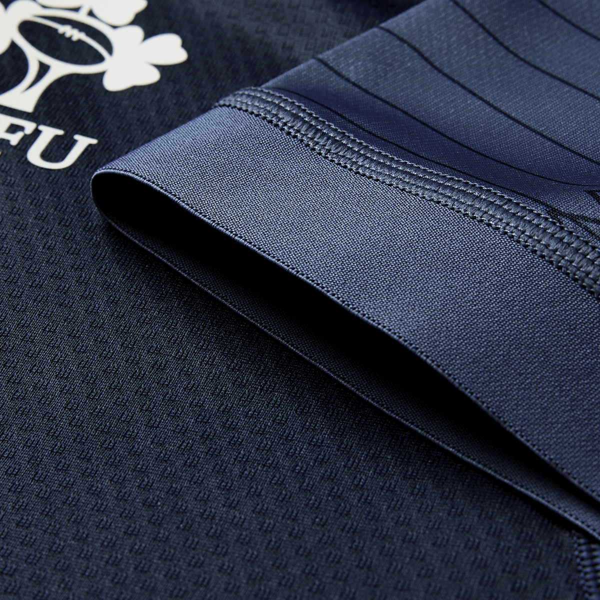 Close-up of the Ireland 26/27 Summer Tour "Indigo" Training Test Jersey by Canterbury shows textured navy fabric, detailed stitching, and part of a white "FU" logo—ideal as an Ireland rugby jersey or for the Summer Tour Test Fit.
