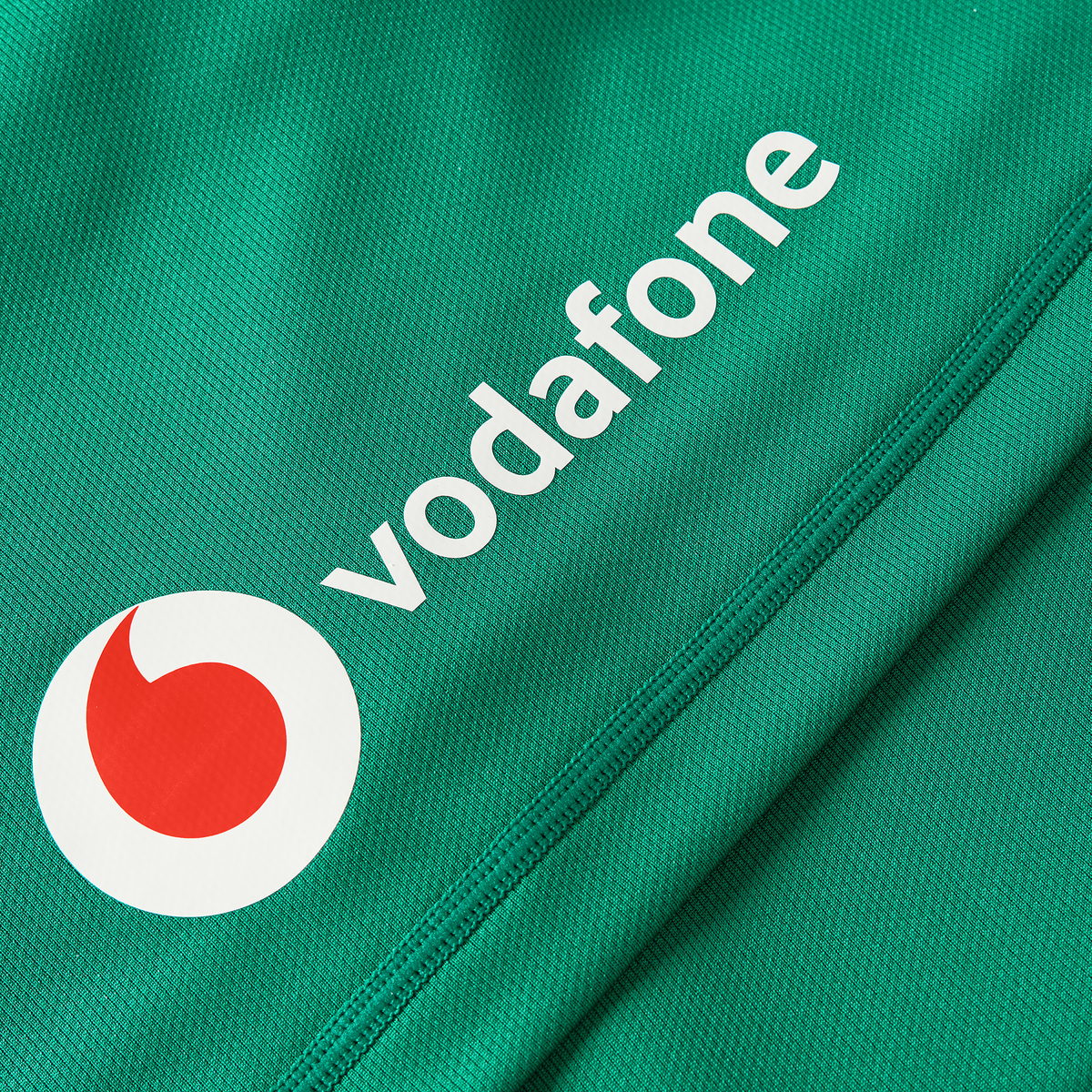 Close-up of green fabric from the Women&#39;s Ireland WIRFU 25/26 Pro Home Jersey by Canterbury, showing white Vodafone text and logo with a red-and-white circular emblem.