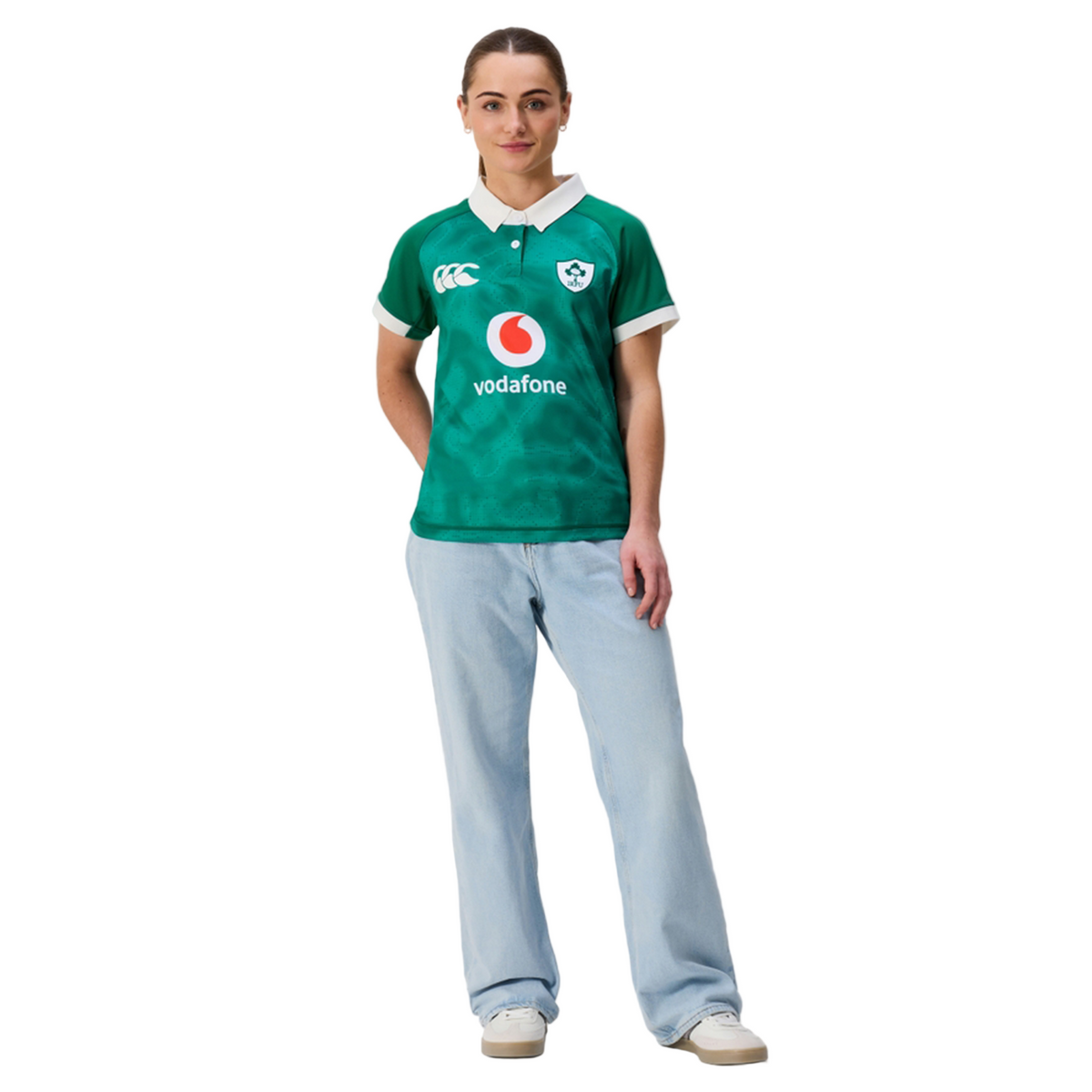 A person stands facing forward, wearing the Canterbury Women&#39;s Ireland 25/26 Home Pro Jersey with light blue jeans and white sneakers against a plain white background.
