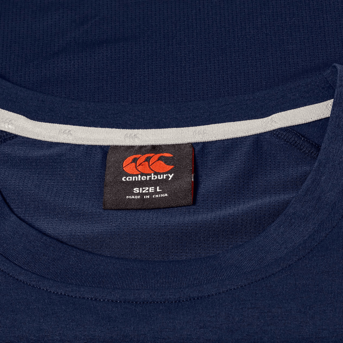 Close-up of a Canterbury Everest Dart Tech T-Shirt in navy blue, showing the inside neck label with the Canterbury logo, size L, and "Made in China" text.