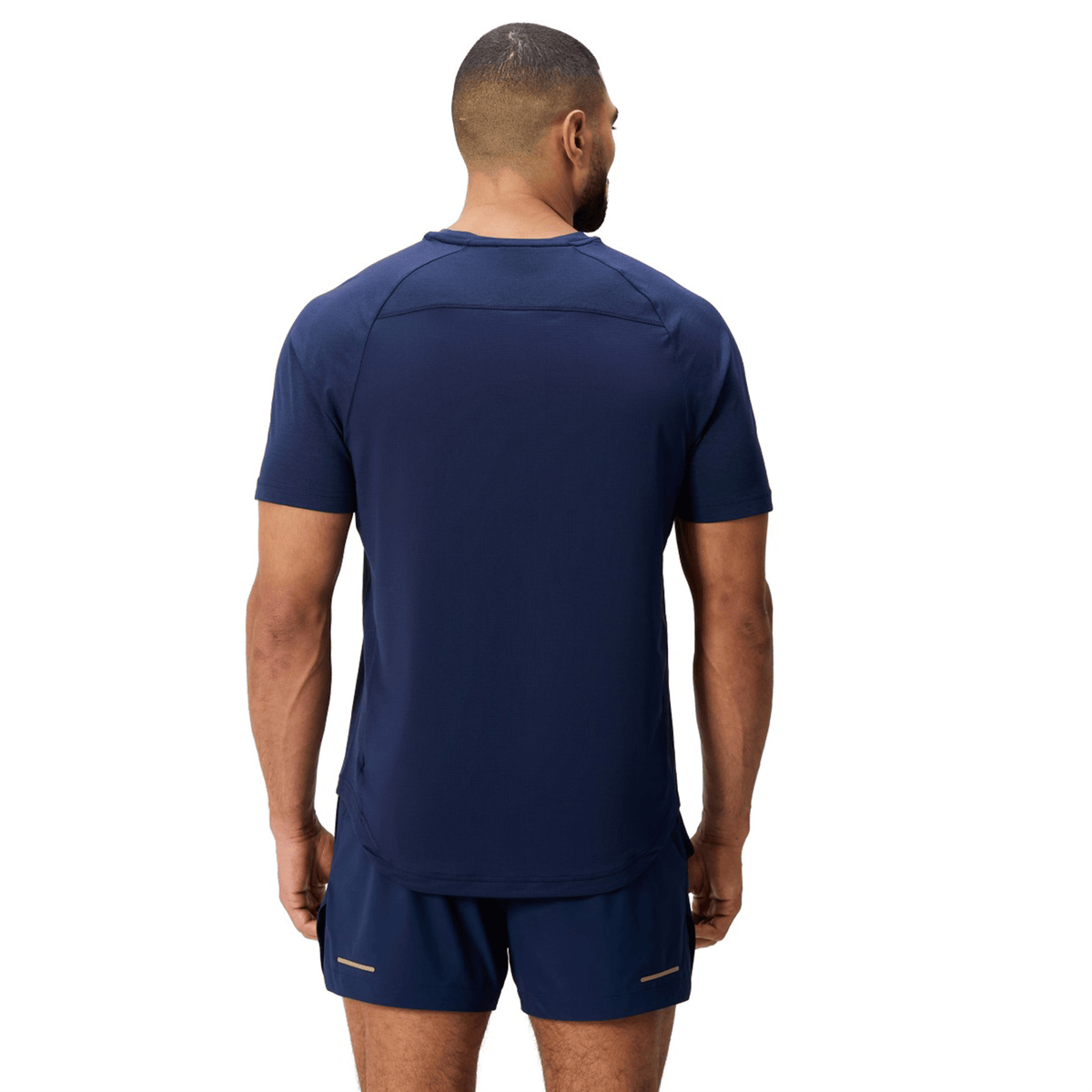 A man faces away from the camera, wearing the Canterbury Everest Dart Tech T-Shirt by Canterbury in navy blue, paired with matching shorts. The moisture-wicking polyester set is displayed against a white background.