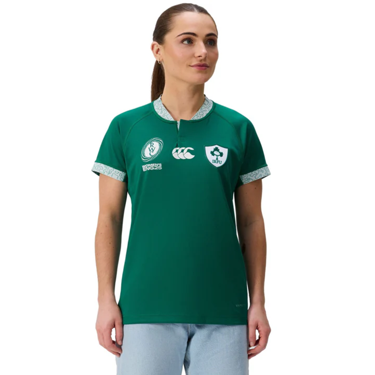 A woman wears the Canterbury Women&#39;s Ireland WRWC25 Replica Home Jersey with sponsor logos and light blue jeans, facing slightly left against a plain white background.