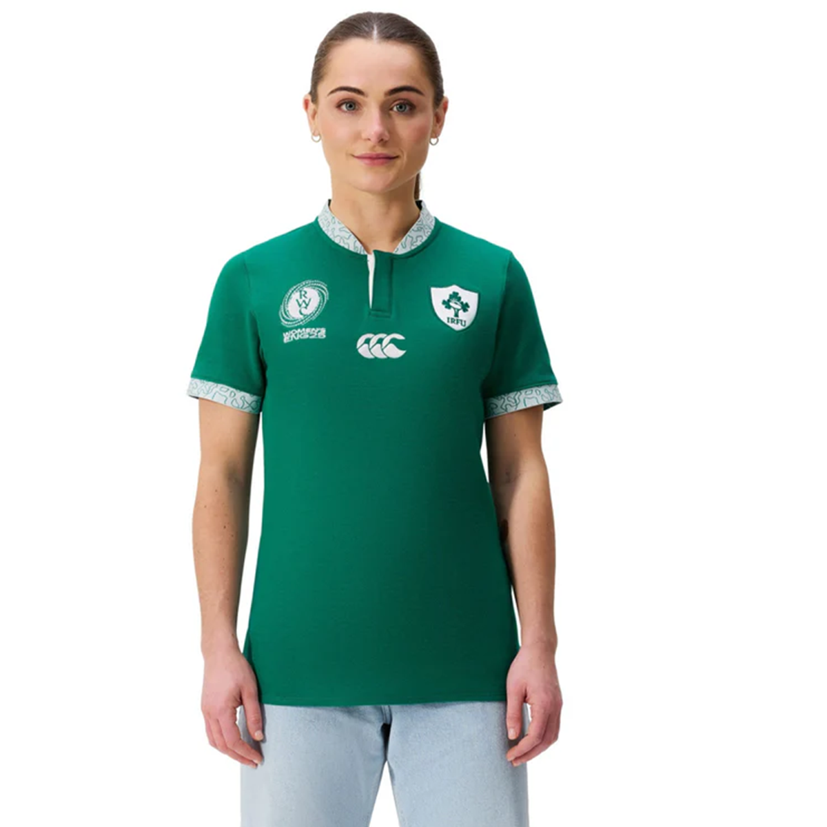 A person wearing the Women&#39;s Ireland WRWC25 Classic Jersey by Canterbury with chest logos and light blue jeans stands facing forward against a white background.