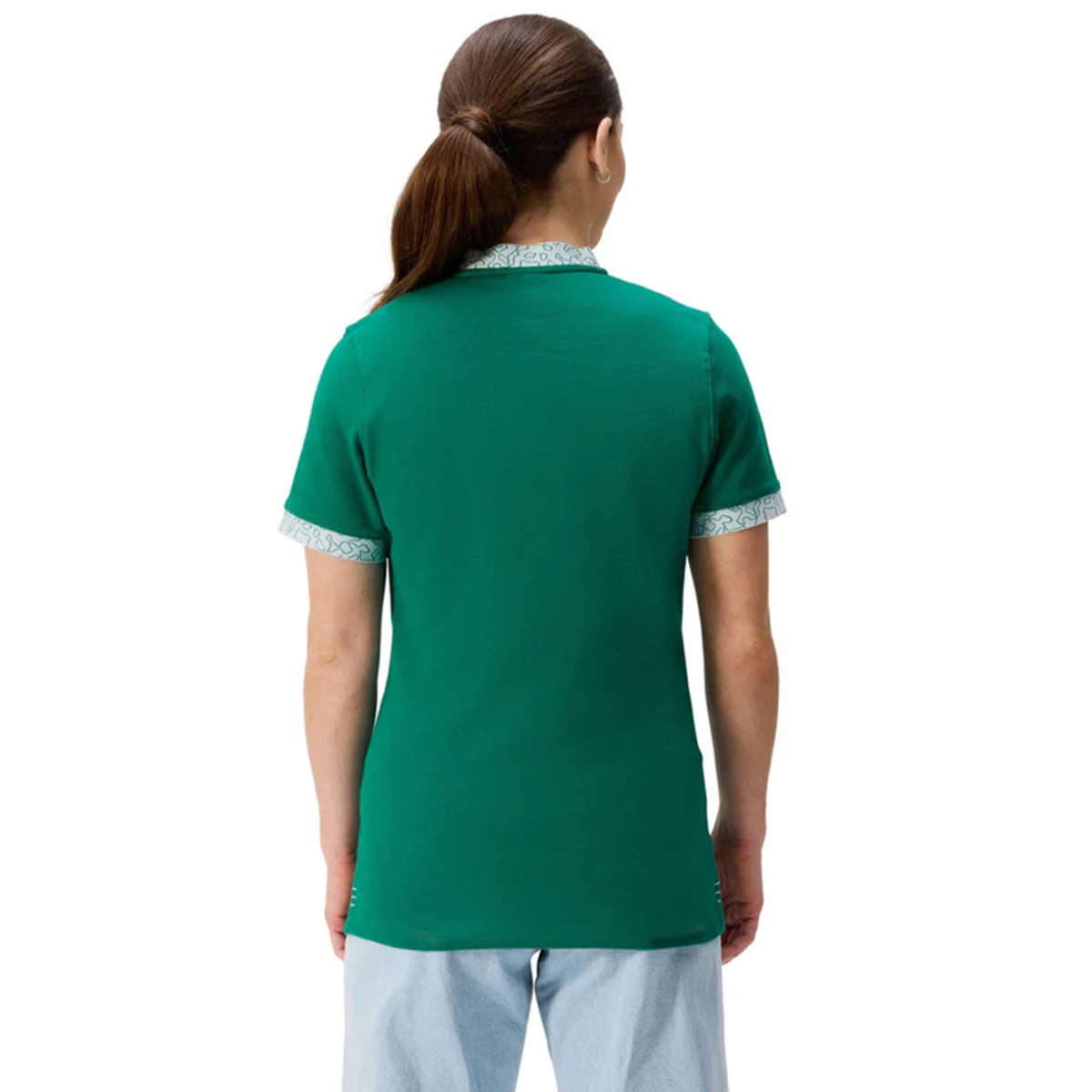 A woman with long brown hair in a ponytail stands facing away, wearing the Canterbury Women&#39;s Ireland WRWC25 Classic Jersey with patterned trim and light blue pants.