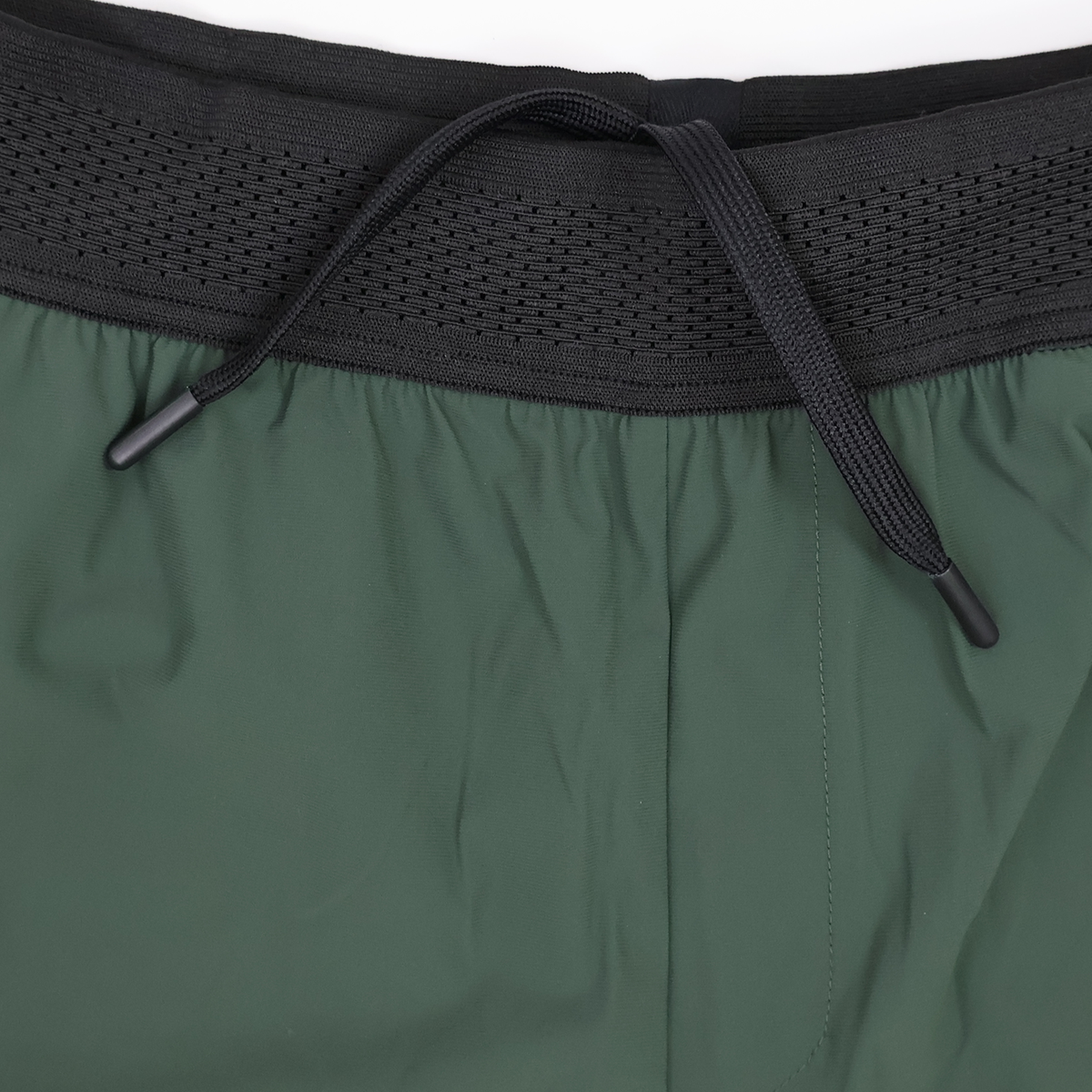 Close-up of the waistband of green Canterbury Everest Woven Short 5" athletic shorts, featuring a black elastic band and center-tied drawstring. Made from four-way stretch fabric for comfort during training. Brand: Canterbury.