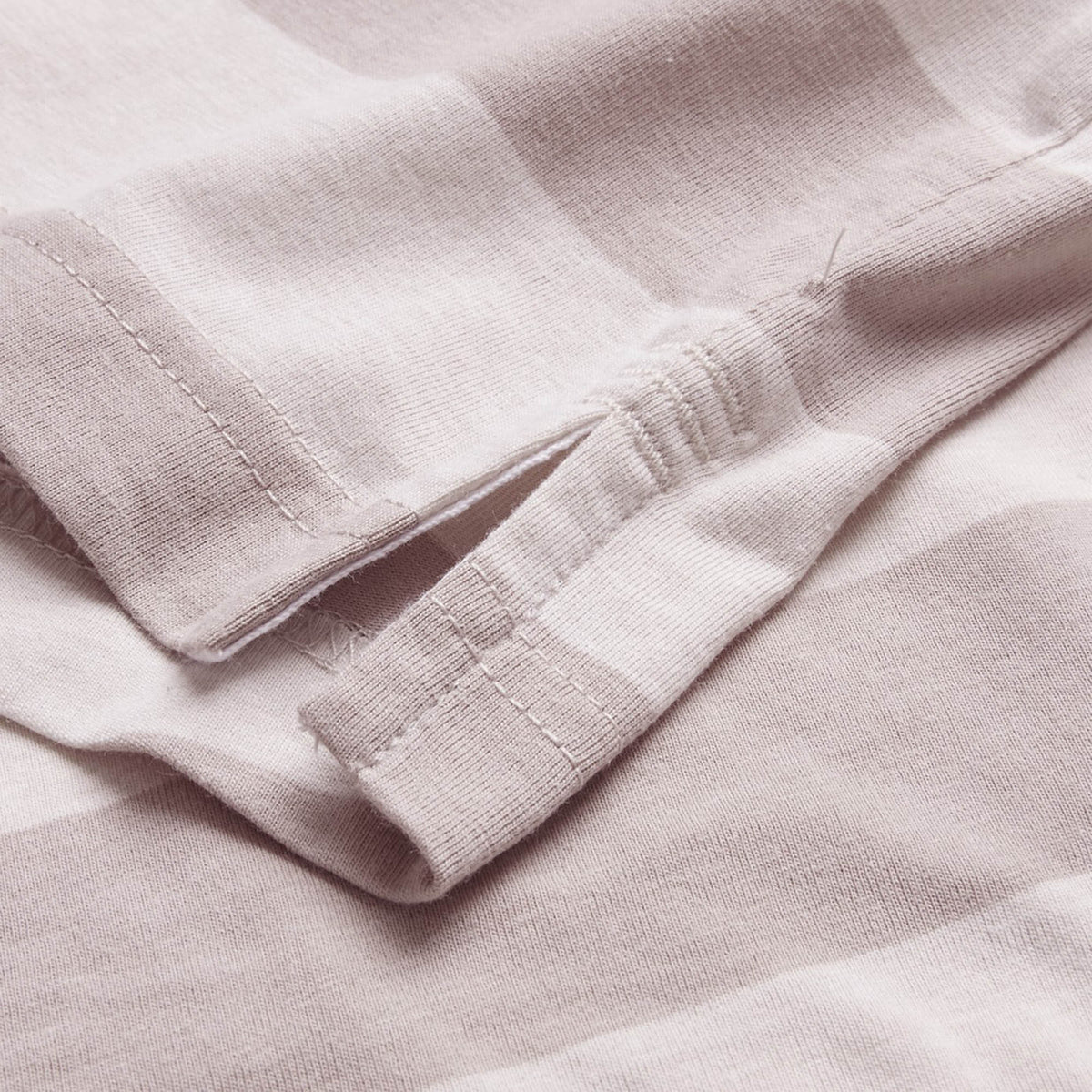 Close-up view of the side seam of the Canterbury Yarn Stripe Polo by Canterbury in a light color, highlighting its classic rugby-inspired design with a small side slit and prominent stitching details.