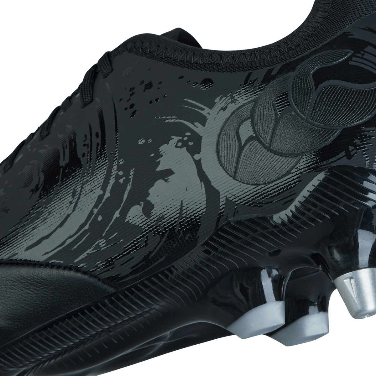 Close-up of the Canterbury Phoenix Genesis Pro SG - Black/Silver Metallic soccer cleat featuring a textured, glossy design and silver studs on the sole for optimal traction in soft ground conditions.
