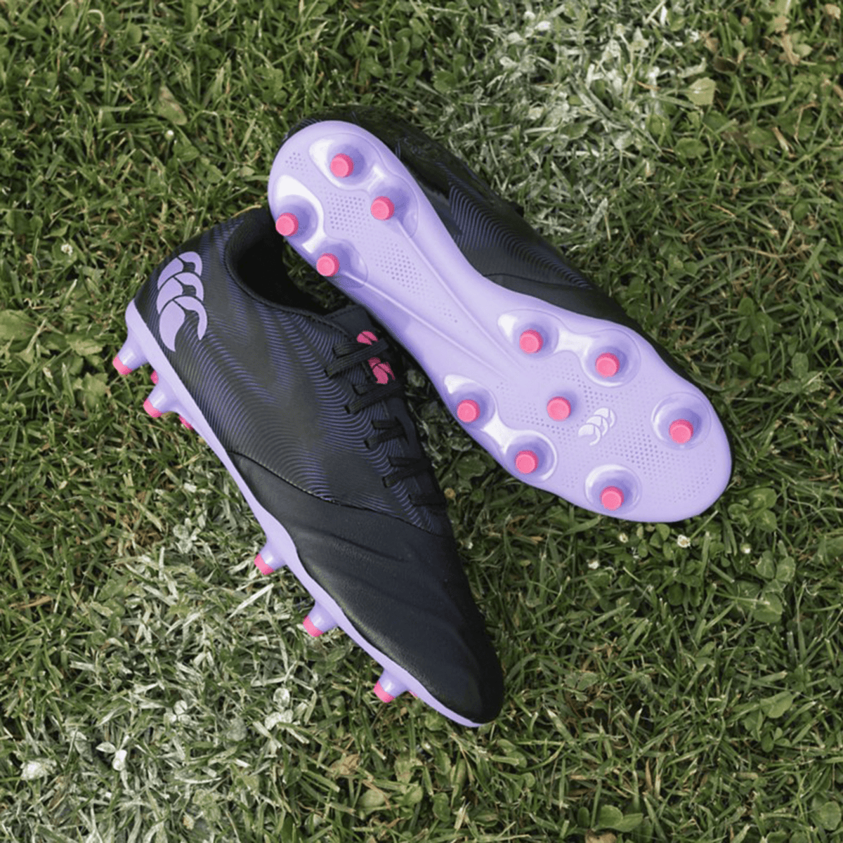 A pair of Canterbury Phoenix Genesis Team FG soccer cleats with pink accents and a synthetic leather forefoot on a grass surface.