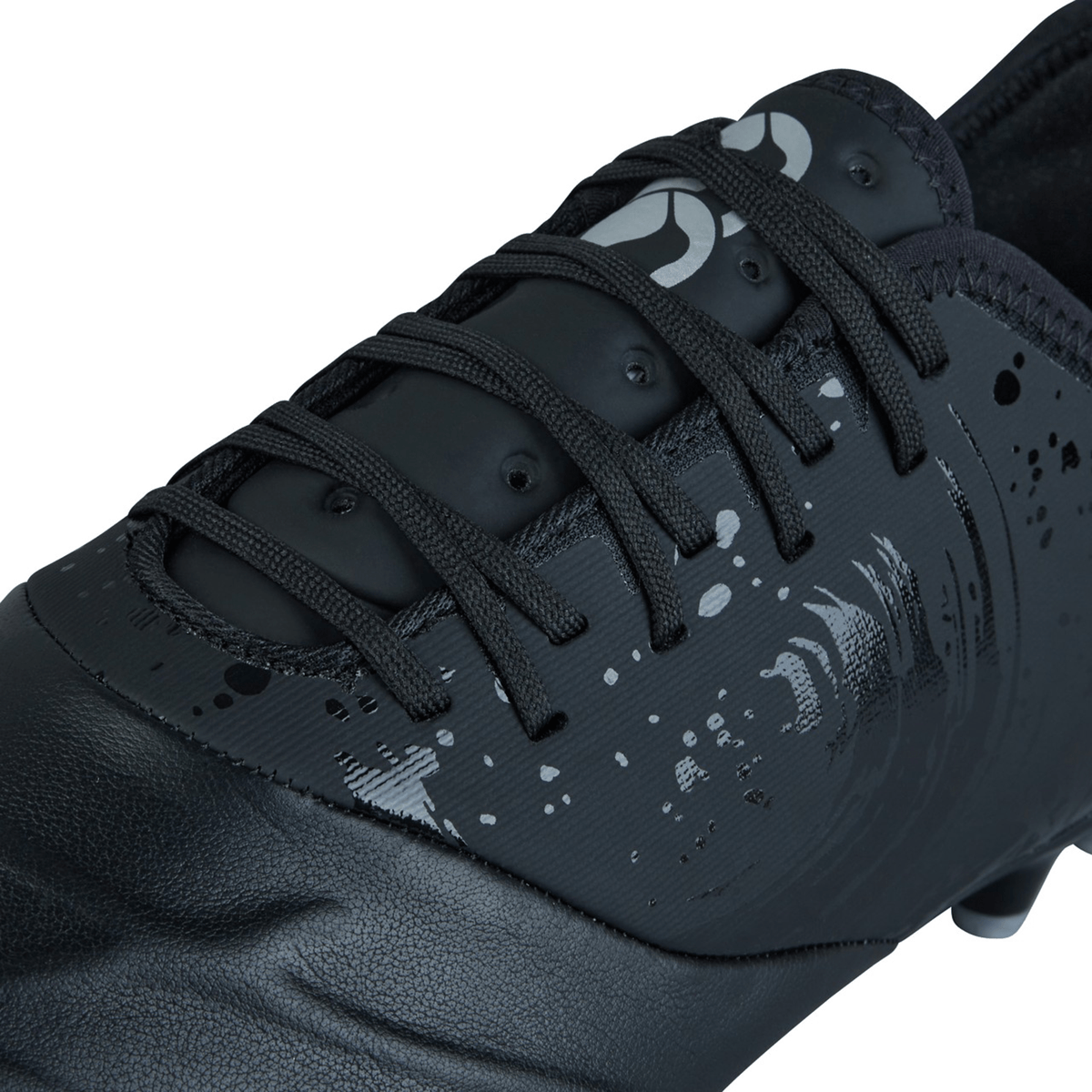 Close-up view of a Canterbury Phoenix Genesis Pro FG athletic shoe in black/silver metallic with black laces and a sleek, modern design featuring TPU-reinforced mesh.