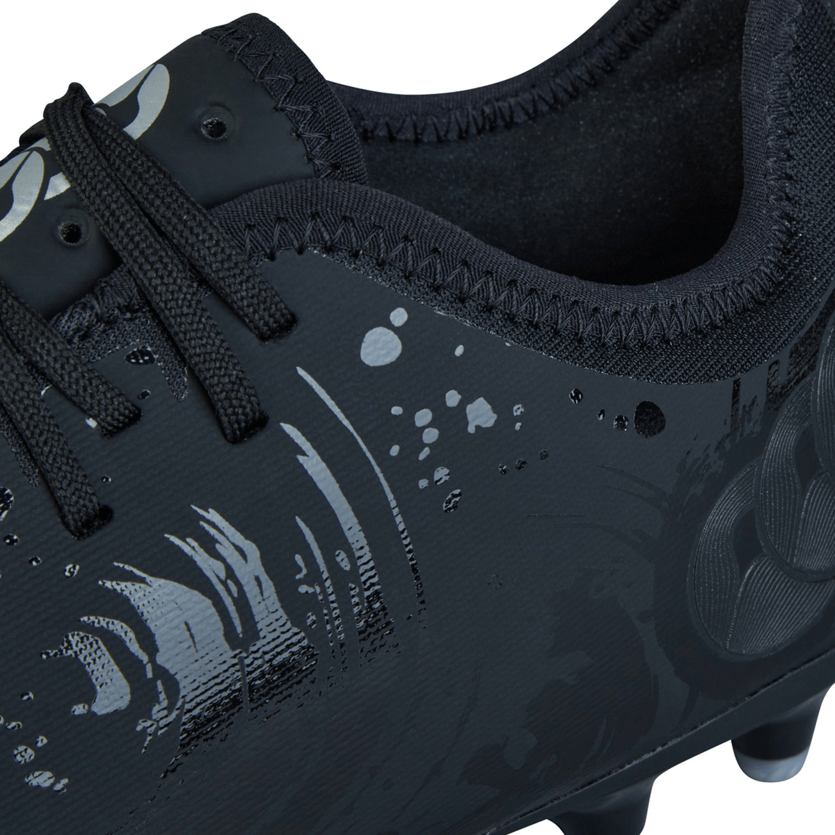 Close-up of a black sports shoe, featuring intricate reflective patterns and black laces. The texture and design details are prominently displayed, highlighting the craftsmanship of the Canterbury Phoenix Genesis Pro FG - Black/Silver Metallic with its TPU-reinforced mesh and firm-ground design.