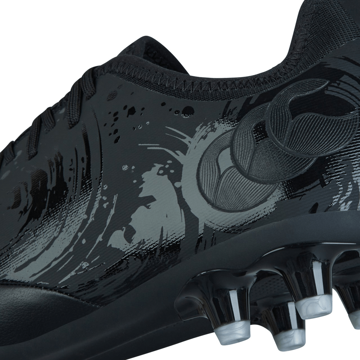 Close-up of a black Canterbury Phoenix Genesis Pro FG - Black/Silver Metallic football boot featuring a sleek design with abstract patterns, TPU-reinforced mesh on the side panel, and molded cleats on the firm-ground sole.