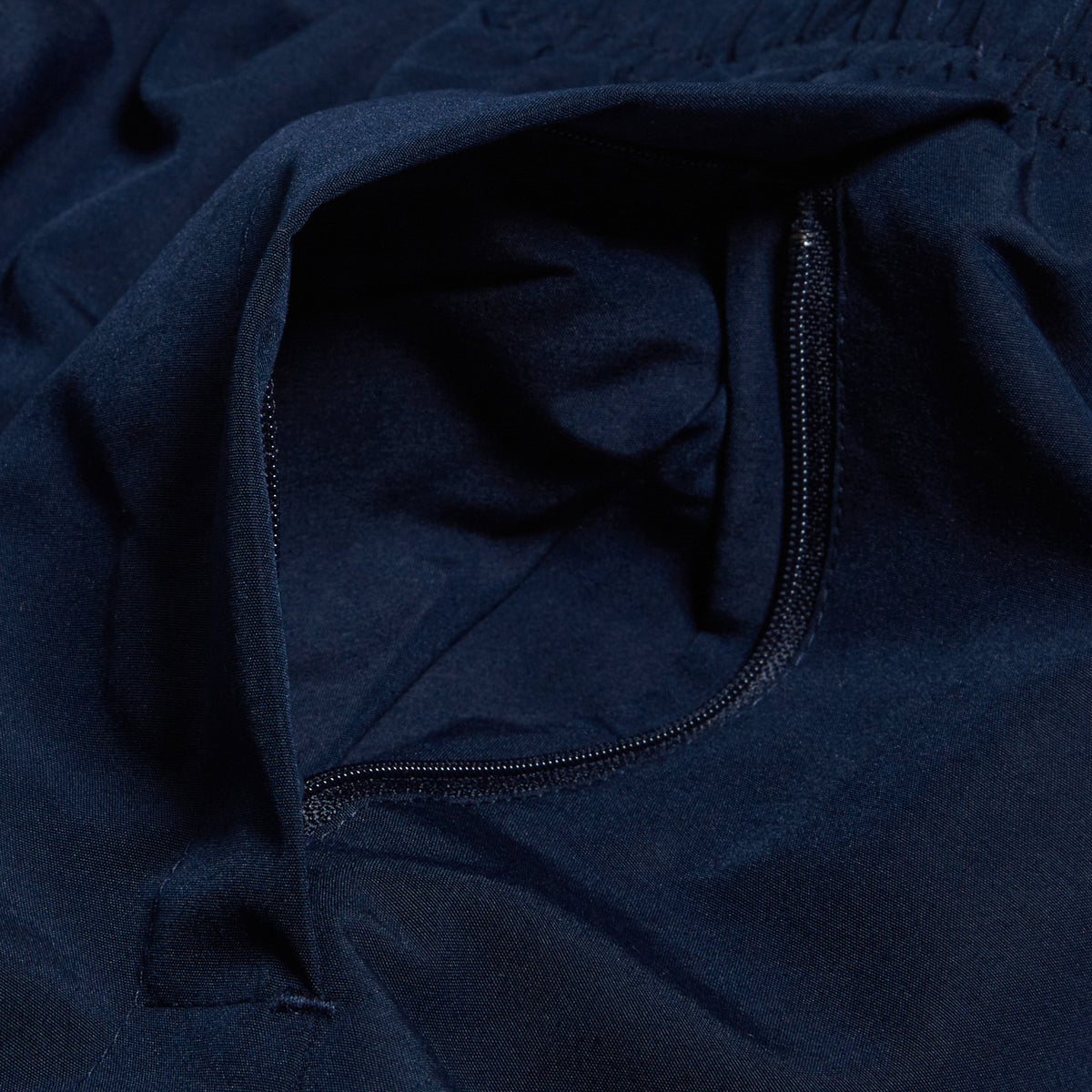 A detailed view of the Women&#39;s Canterbury Open Hem Stadium Pant showcases a navy blue fabric with an unzipped pocket, ideal for rugby training. The Canterbury logo adds a touch of authenticity and style to the design.
