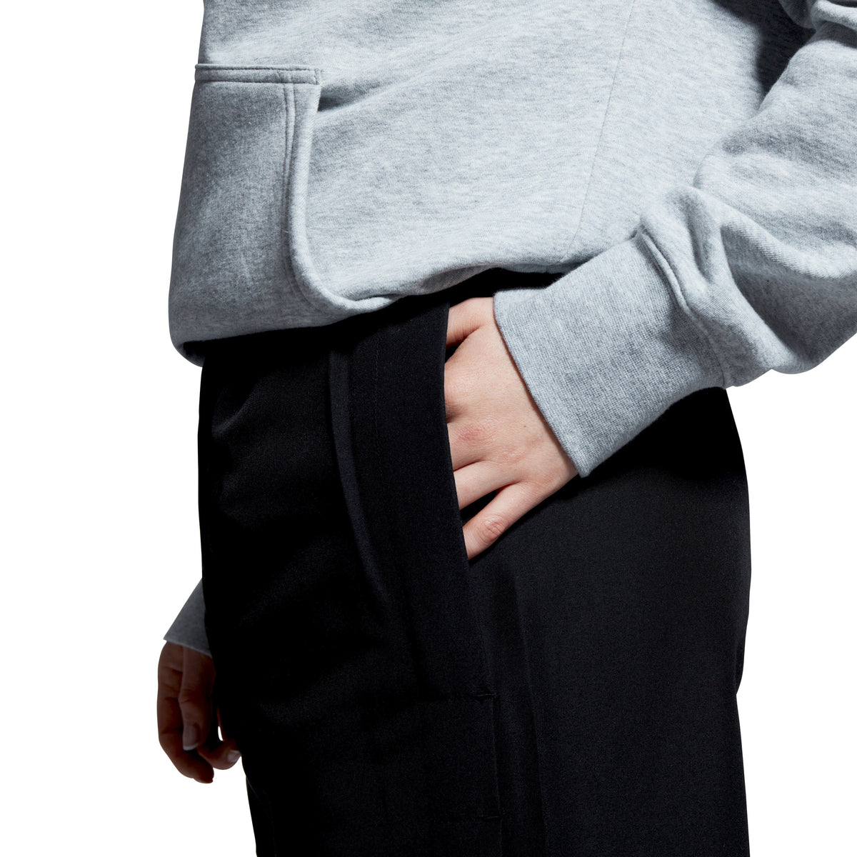 A person wearing a gray hoodie and Women&#39;s Canterbury Open Hem Stadium Pant in black, featuring full-length leg zips, with one hand casually tucked in the pant pocket.