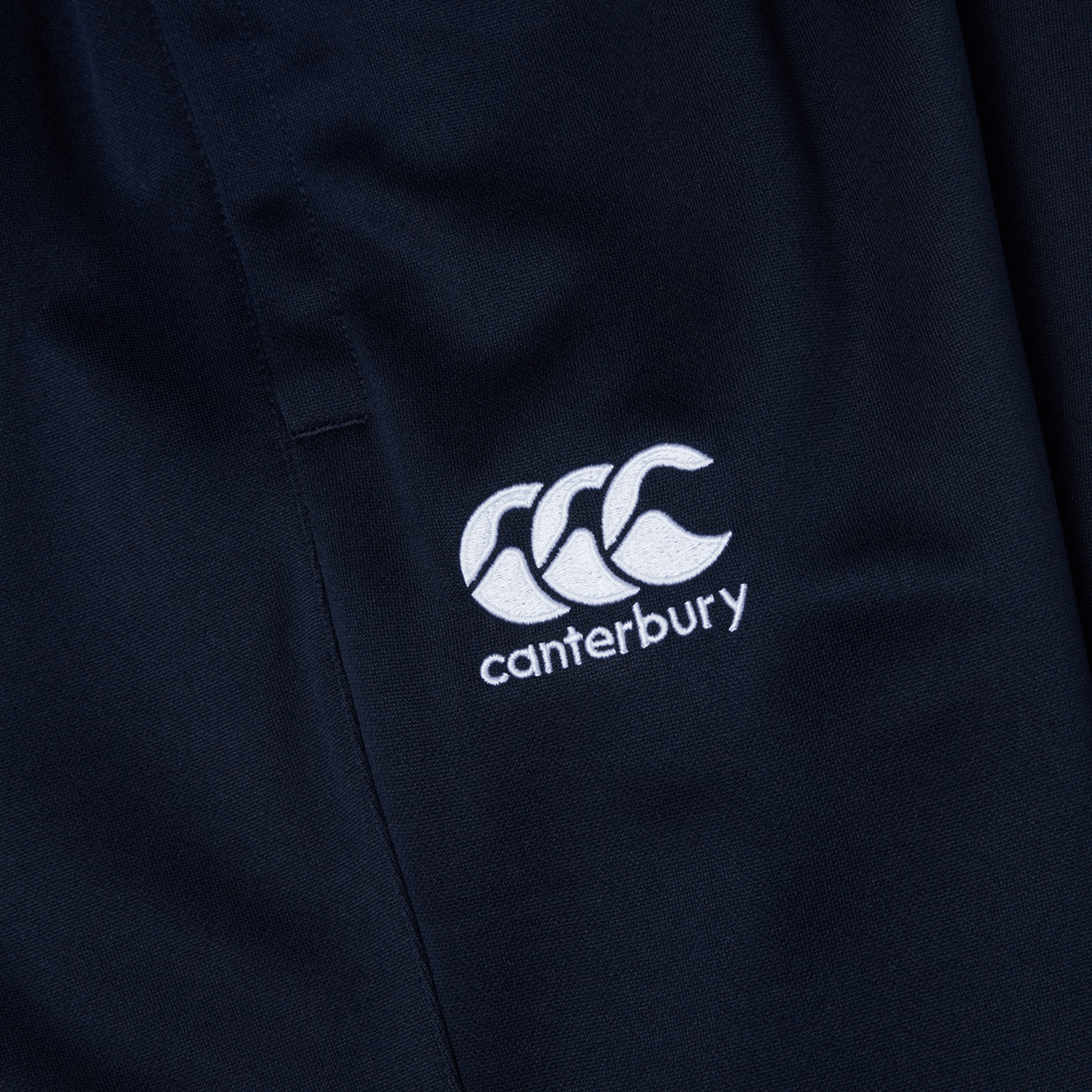 Close-up of navy blue fabric with a white embroidered logo of three overlapping figures and the text &quot;Canterbury&quot;—perfect for Canterbury Stretch Tapered Pants that are quick-dry and ideal for your workout.