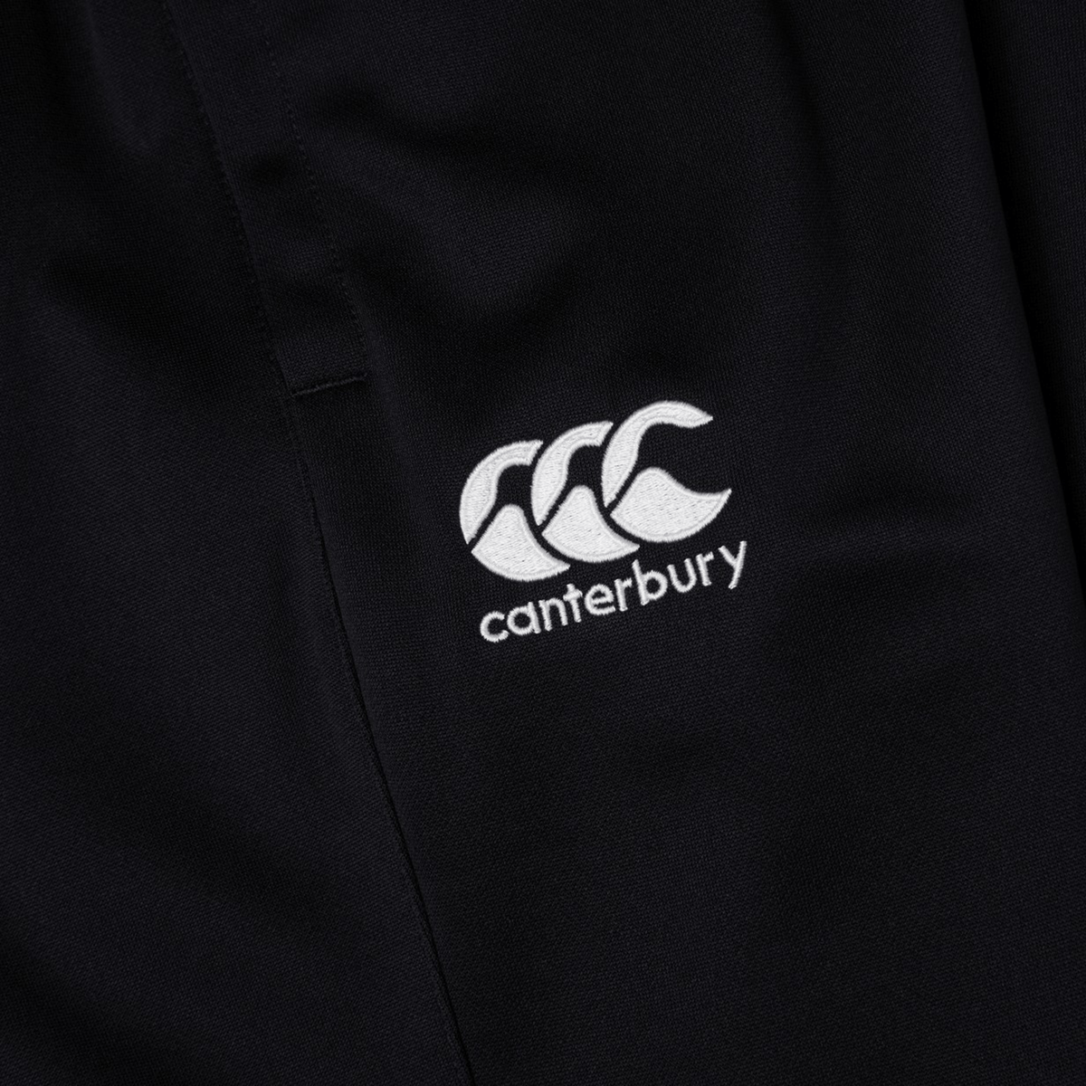 Close-up of black fabric with an embroidered white &quot;Canterbury&quot; logo, perfect for the Canterbury Stretch Tapered Pant by Canterbury.