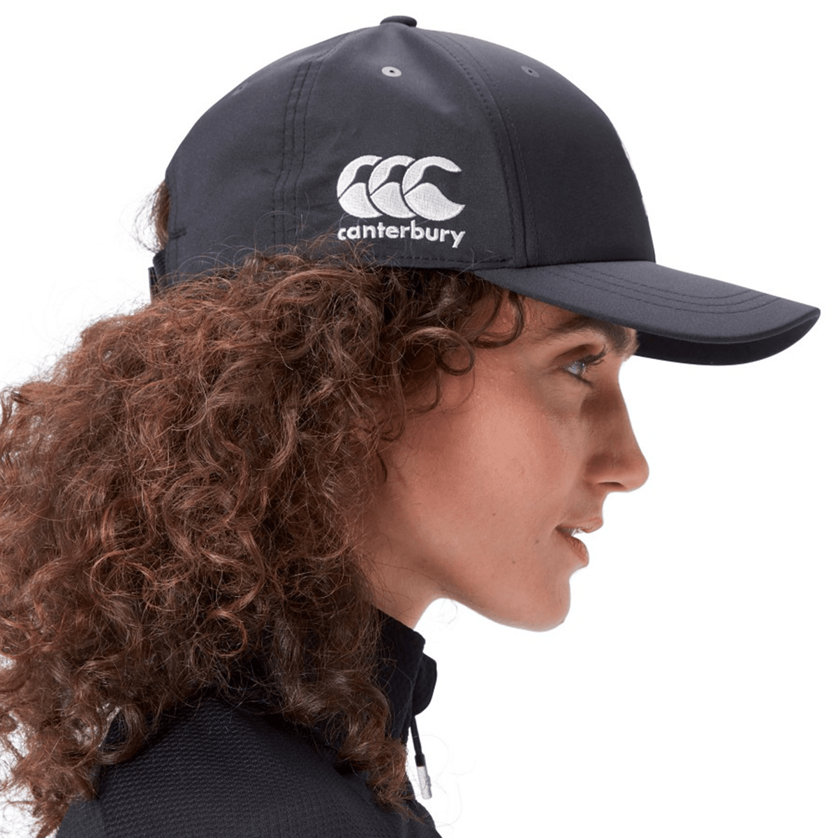 Person with curly hair wears a black Ireland 25/26 Tech Logo Cap by Canterbury, photographed in profile against a plain background.