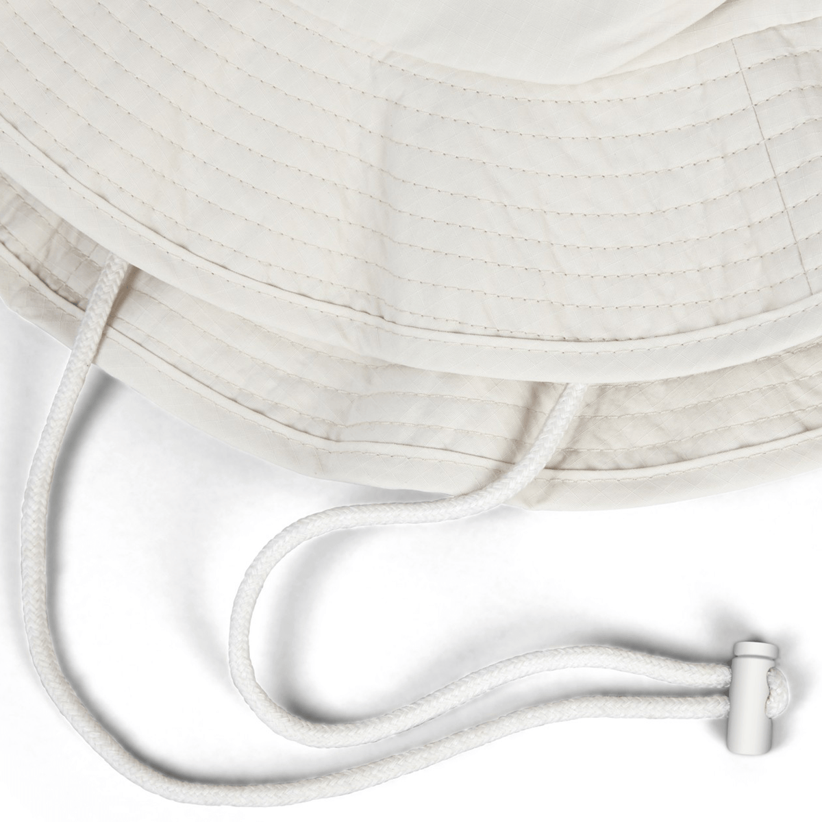 The British &amp; Irish Lions 2025 Outback Wide Brim Bucket Hat by Canterbury is showcased in a close-up, highlighting its beige quilted design. The hat features a white adjustable drawstring with a toggle against a white background and is crafted from quick-dry ripstop fabric for superior comfort and durability.