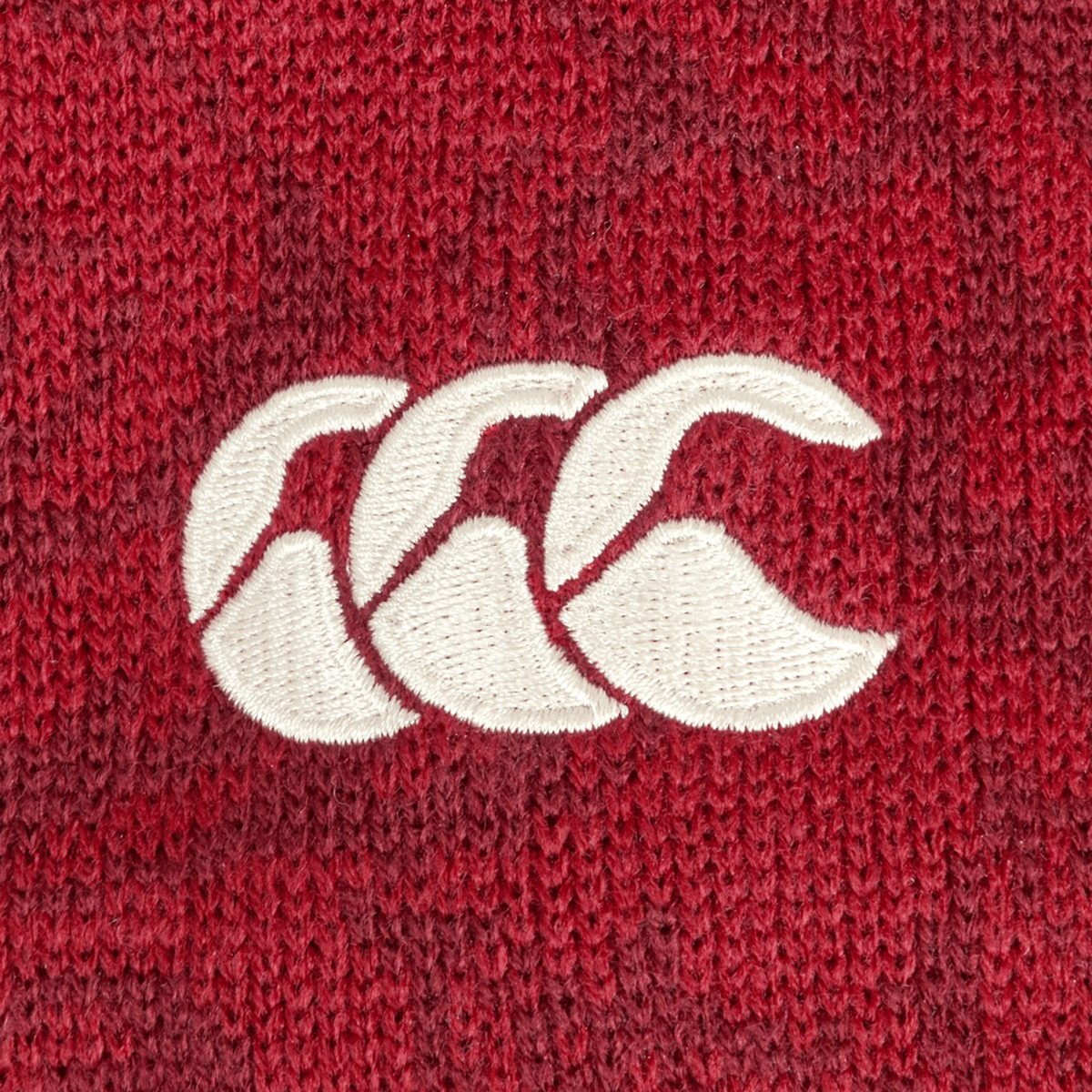 Close-up of a red knitted fabric on the British &amp; Irish Lions 2025 Pom-Pom Beanie by Canterbury, featuring a white embroidered logo with three overlapping stylized C's, reminiscent of the renowned Canterbury style.