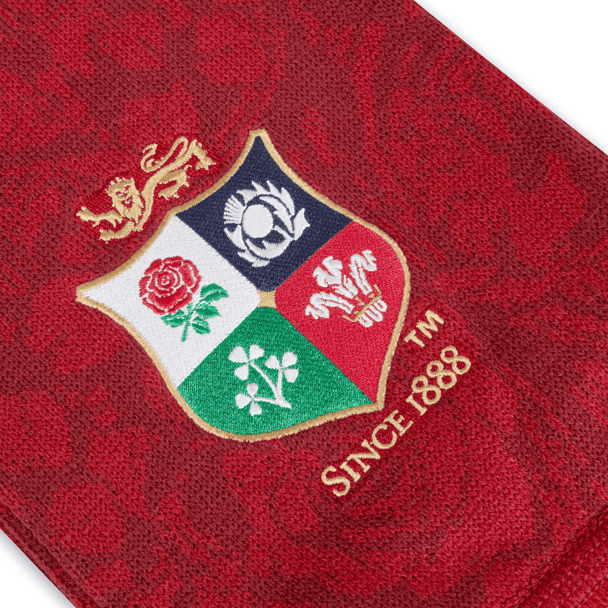 The British &amp; Irish Lions 2025 Supporters Scarf by Canterbury features red fabric adorned with a multicolored embroidered crest displaying four emblems and a lion at the top, reflecting the BIL branding. With text reading "Since 1888," this scarf is an ideal accessory for fans of the British &amp; Irish Lions.