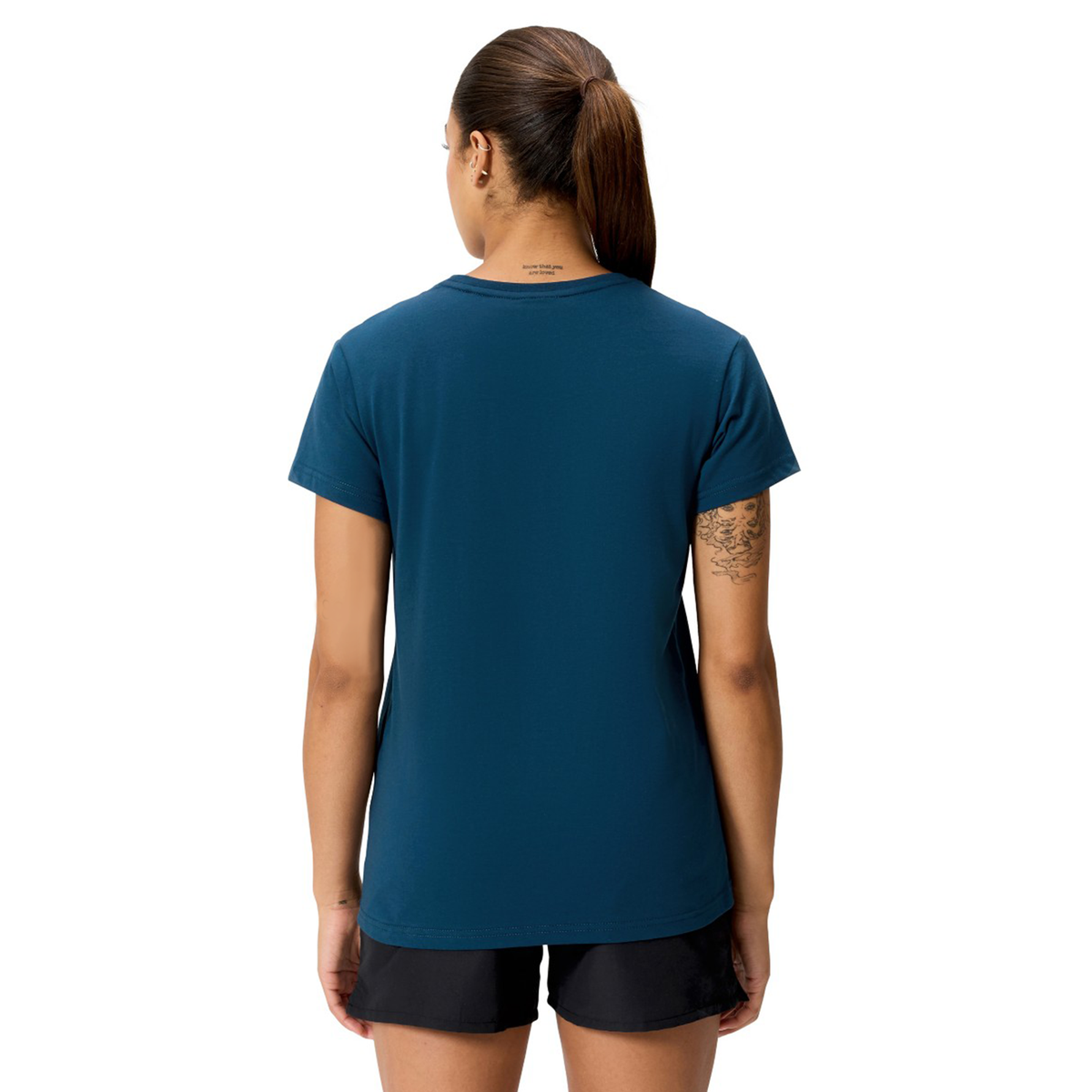A woman with a ponytail, standing with her back to the camera, wears a blue Women&#39;s Uglies Logo T-Shirt by Canterbury and black shorts.