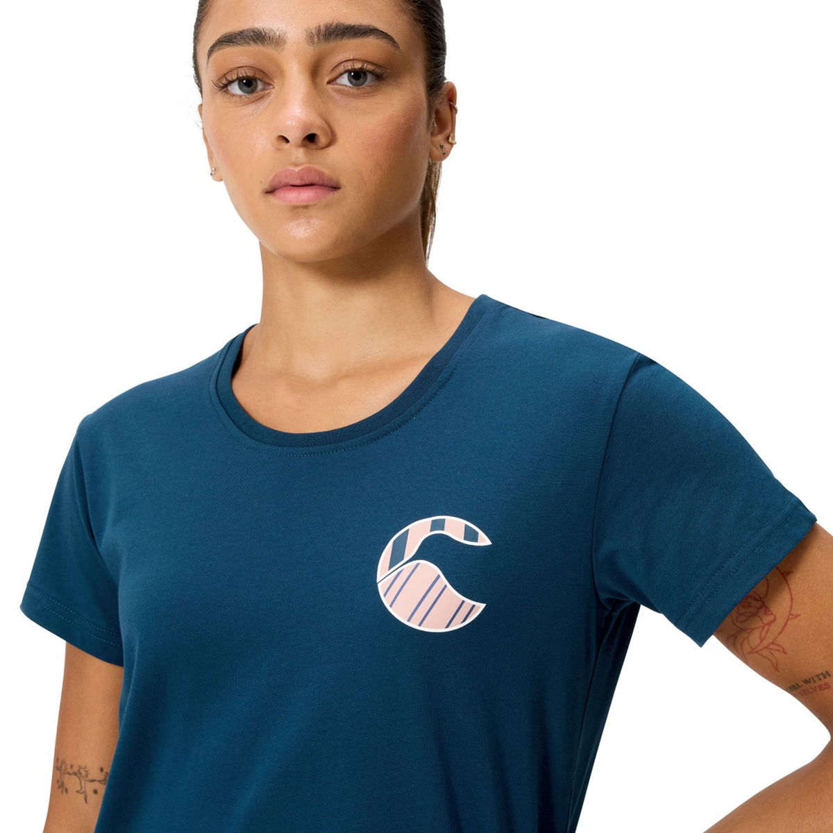 A woman faces the camera in a neutral pose, wearing the Canterbury Women&#39;s Uglies Logo T-Shirt with a bold &quot;C&quot; logo on the chest, highlighting this rugby-inspired women&#39;s apparel from Canterbury.