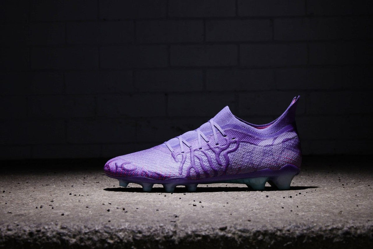 A single Canterbury Speed Infinite Elite FG - Prism Violet/Verbena soccer cleat with a VAPOSKIN membrane against a brick wall background, highlighted by dramatic lighting.